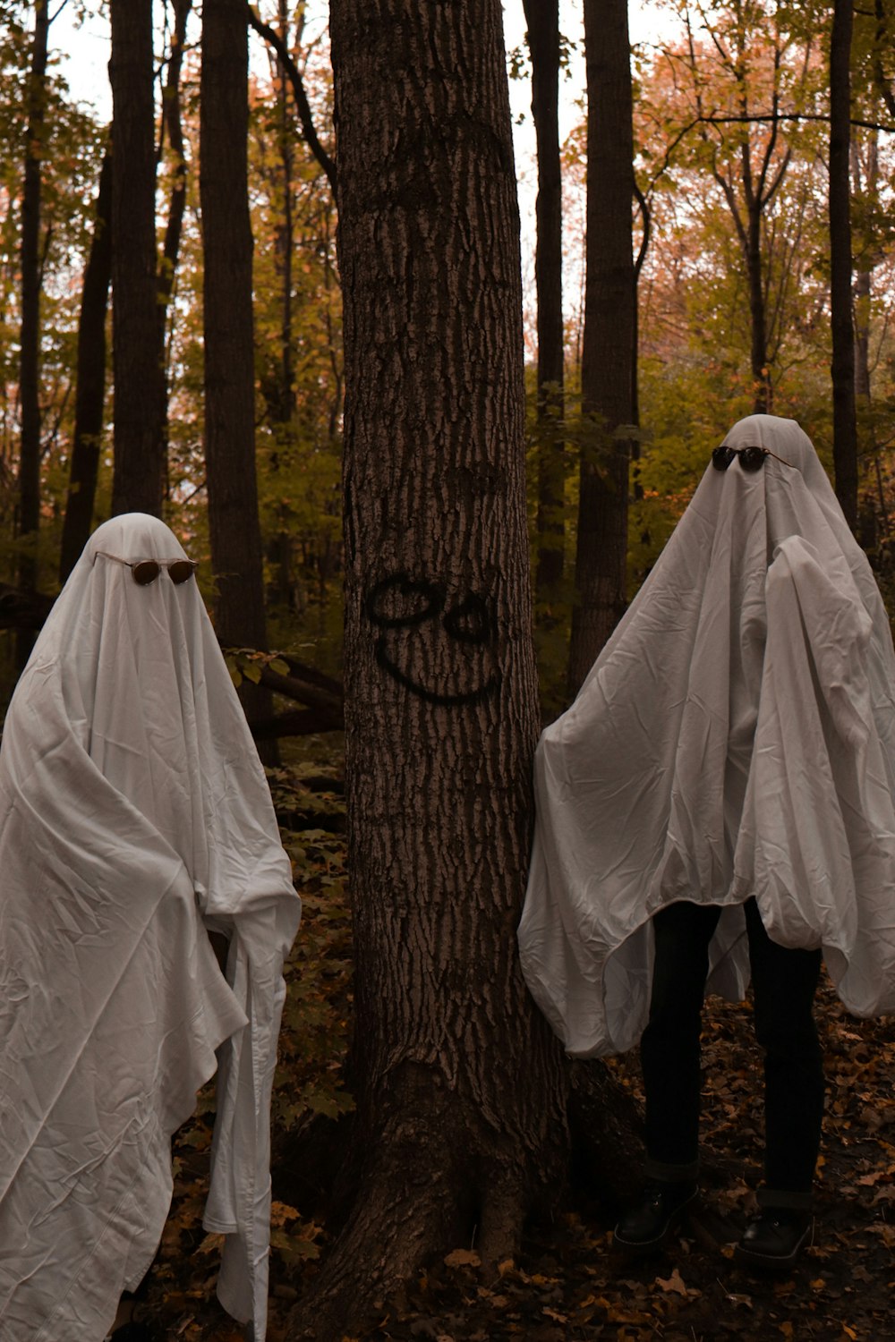 two people in white ghost costumes standing next to a tree