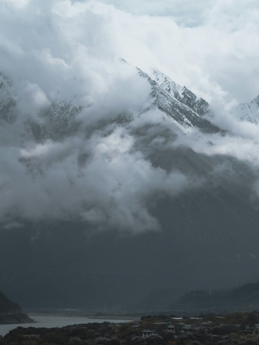 a mountain covered in clouds with a body of water in the foreground