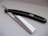A straight razor with a glossy black handle and shiny metal blade, resting on a smooth, light-colored surface.