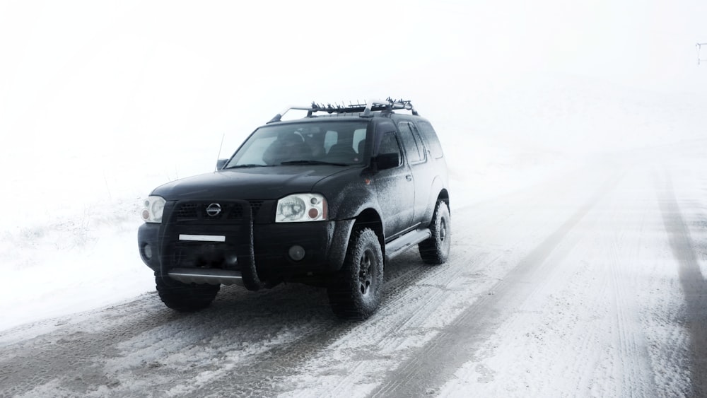 a black suv driving down a snow covered road