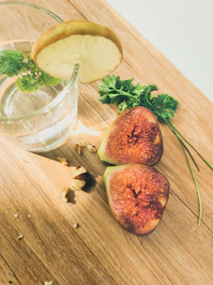 Close-up of a chilled glass of fig lemonade with condensation, surrounded by fresh figs and lemon slices on a wooden table.