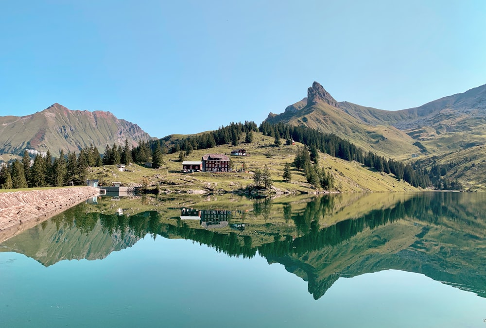 a lake surrounded by mountains with a house on top of it