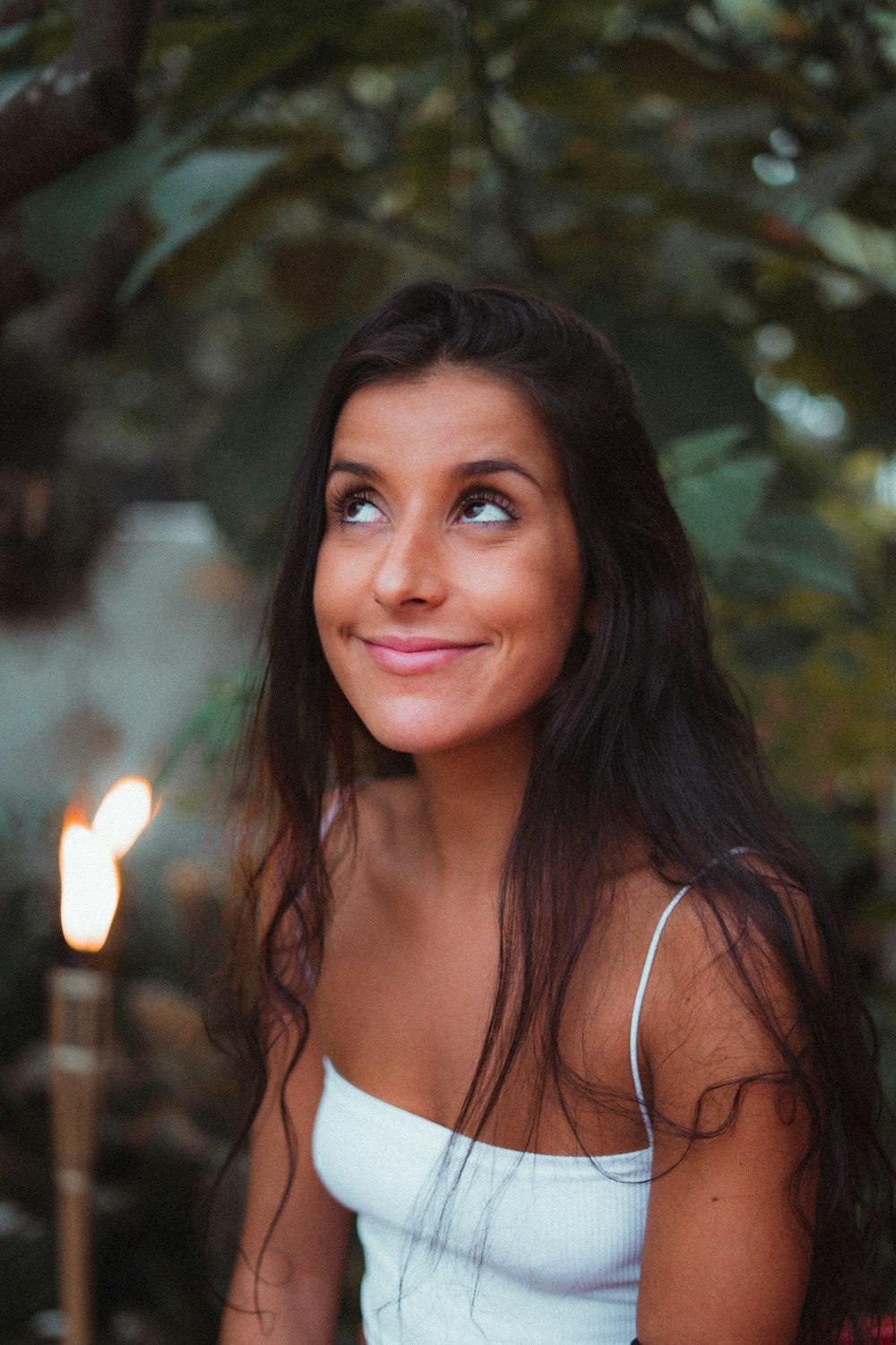 a woman in a white tank top sitting in front of a lit candle