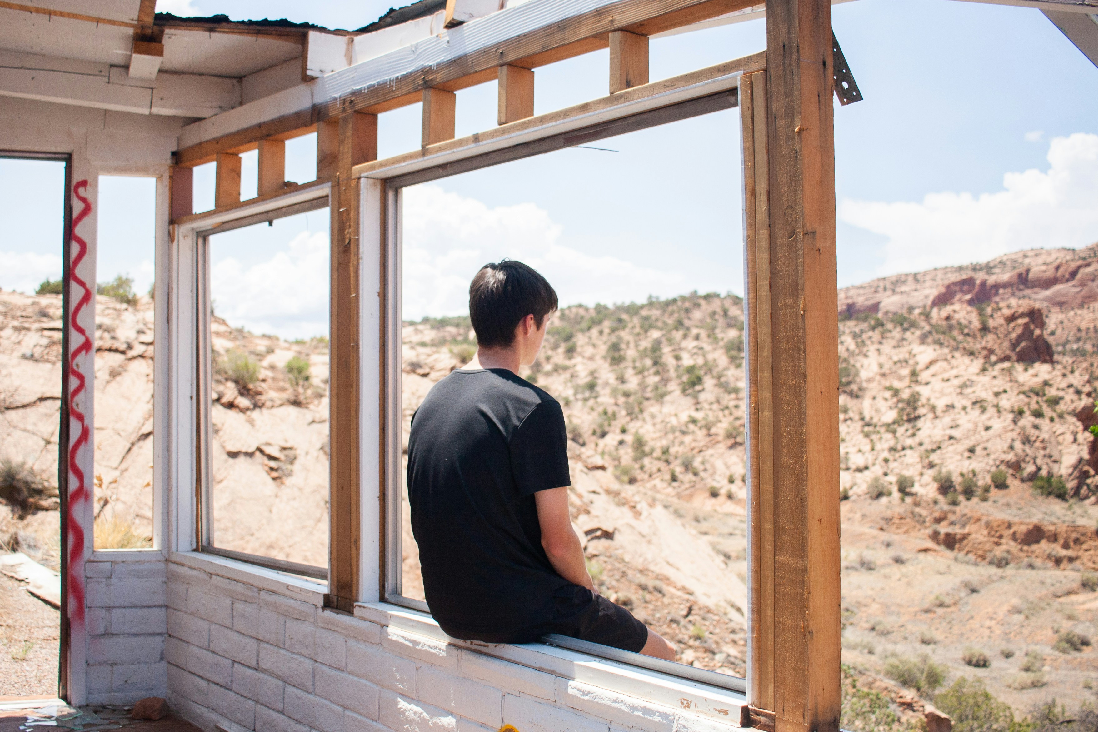 A man sitting on a window sill looking out a window photo – Free Person ...