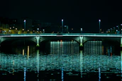 A peaceful bridge illuminated softly at night, reflecting over calm water.