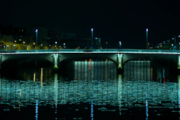 A peaceful bridge illuminated softly at night, reflecting over calm water.