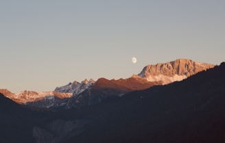 a view of a mountain range with a half moon in the sky