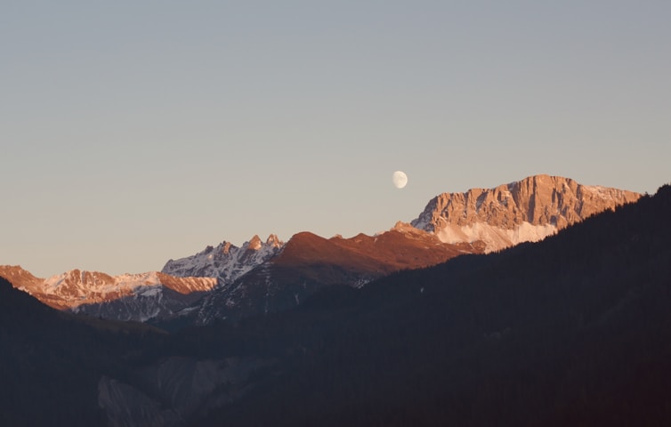 a view of a mountain range with a half moon in the sky