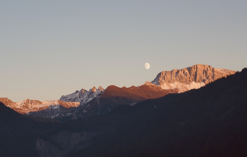 Una vista de una cadena montañosa con media luna en el cielo