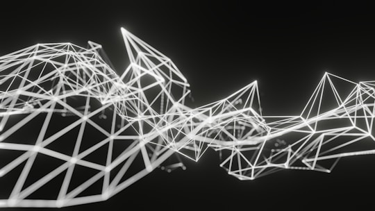 Geometric structures composed of interconnected white lines form an abstract polygonal pattern on a dark background. The lines create various triangular and diamond shapes, giving a sense of three-dimensional depth and complexity.