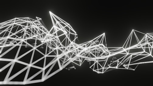 Geometric structures composed of interconnected white lines form an abstract polygonal pattern on a dark background. The lines create various triangular and diamond shapes, giving a sense of three-dimensional depth and complexity.