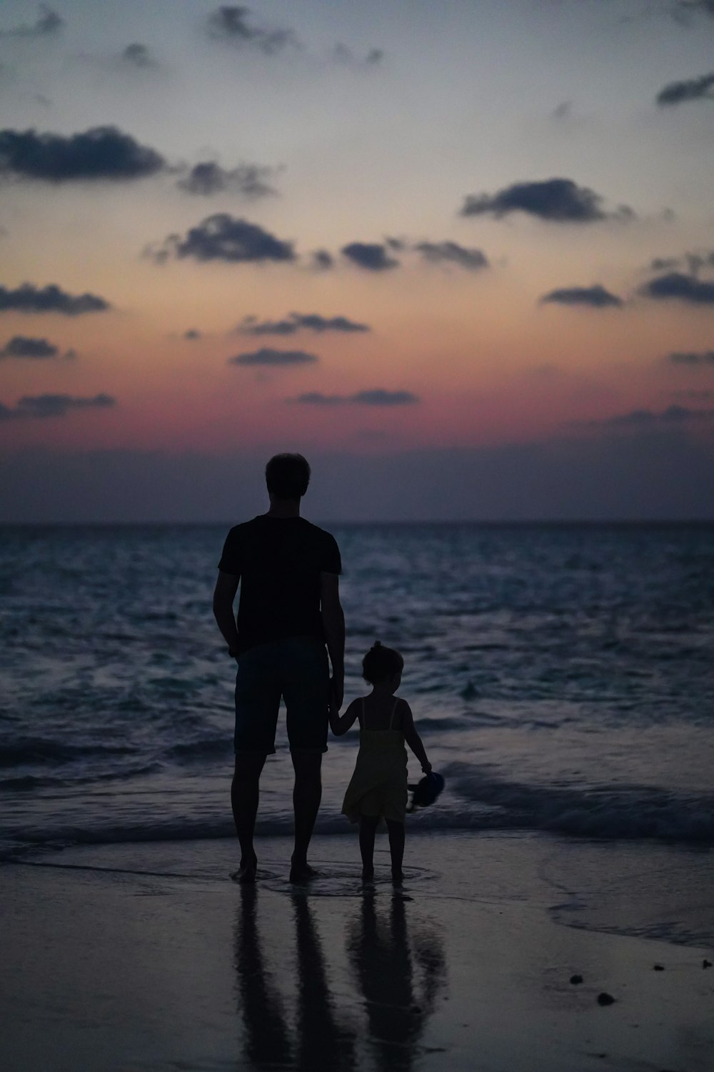 Un hombre y una niña caminando por la playa al atardecer