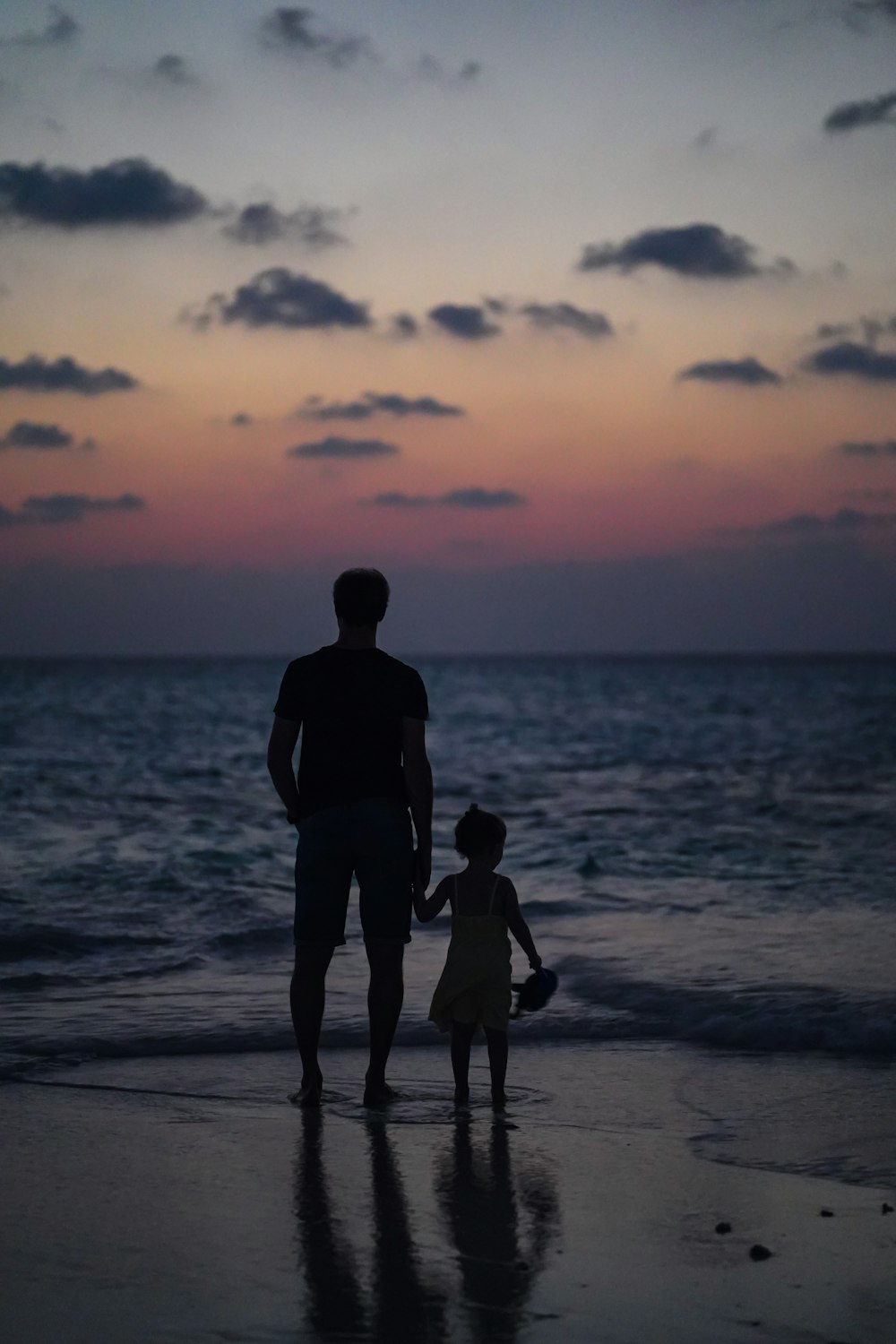 um homem e uma menina que caminham na praia ao pôr do sol