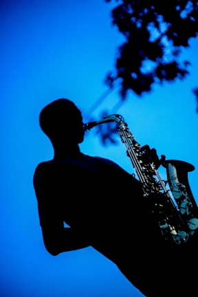 An atmospheric sunset silhouette of a solo musician playing saxophone on an open rooftop.