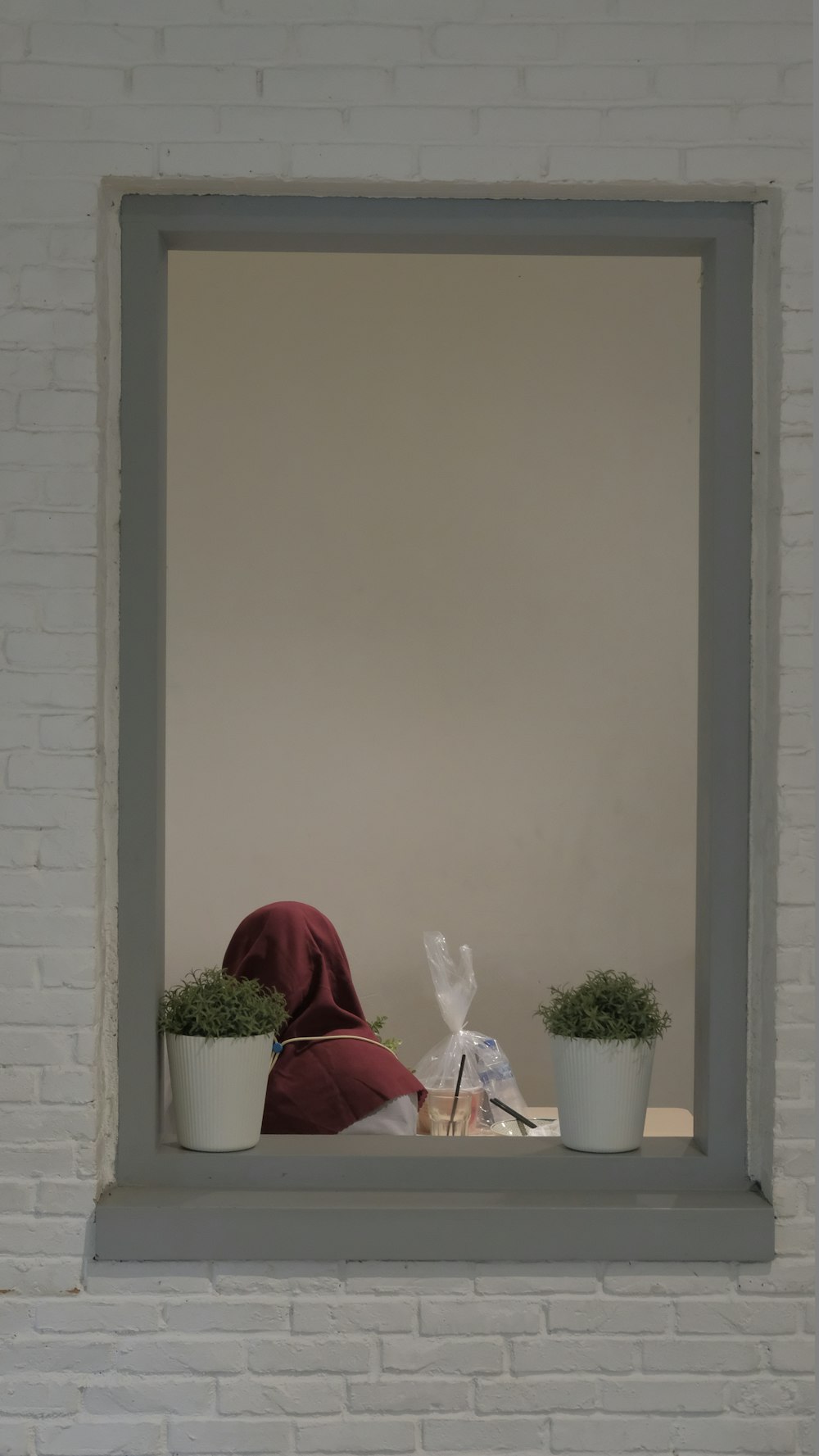 a white brick wall with a window and potted plants