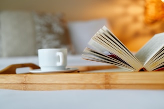 an open book on a bed with a cup of coffee