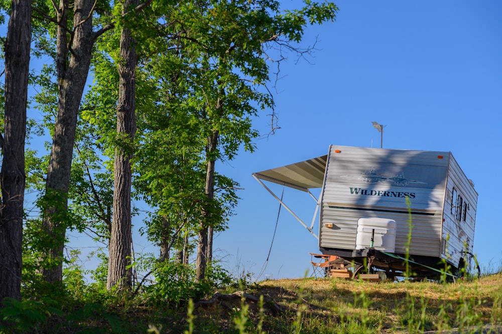 a camper sits on a hill next to some trees