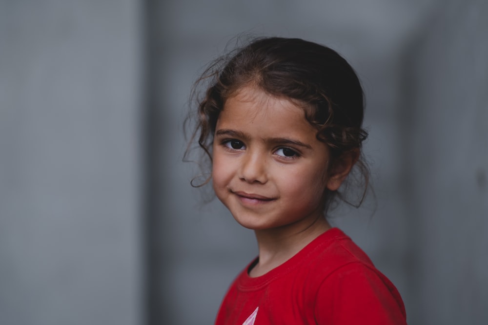 a young girl in a red shirt smiles at the camera