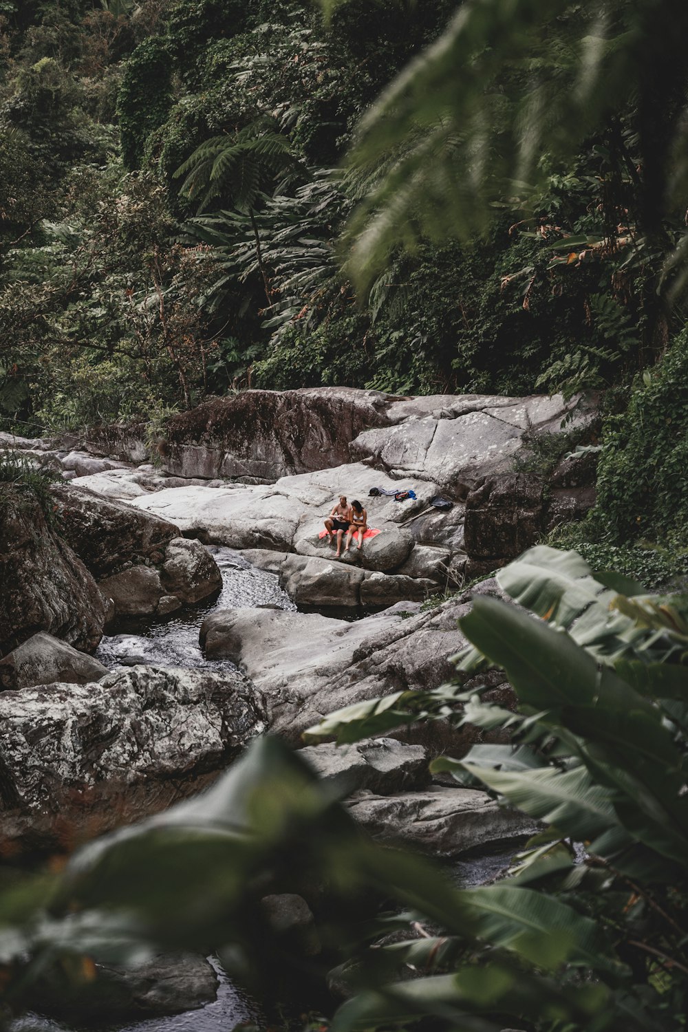 a couple of people sitting on top of a rock next to a river