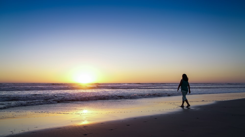 a woman walking along the beach at sunset