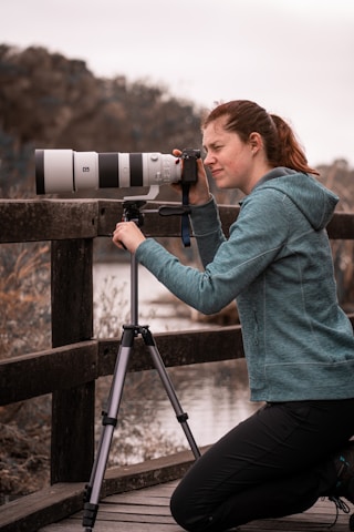 a woman sitting on a bridge looking through a telescope