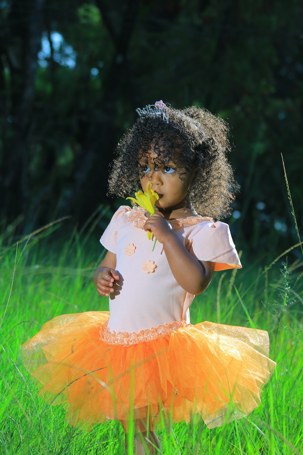 a little girl standing in a grassy field holding a flower
