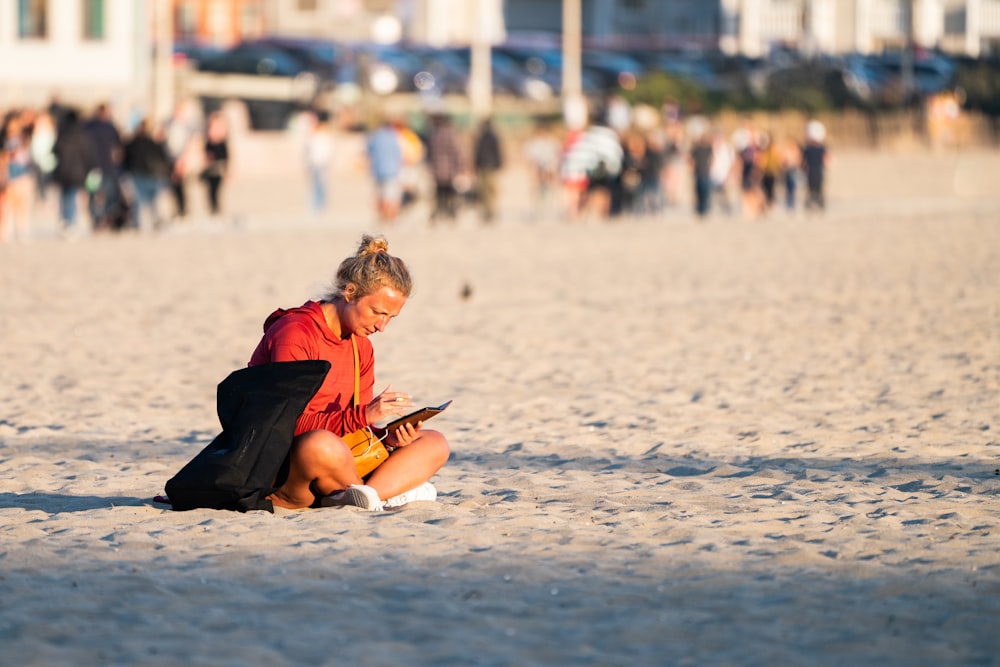 a woman sitting on the beach looking at her cell phone