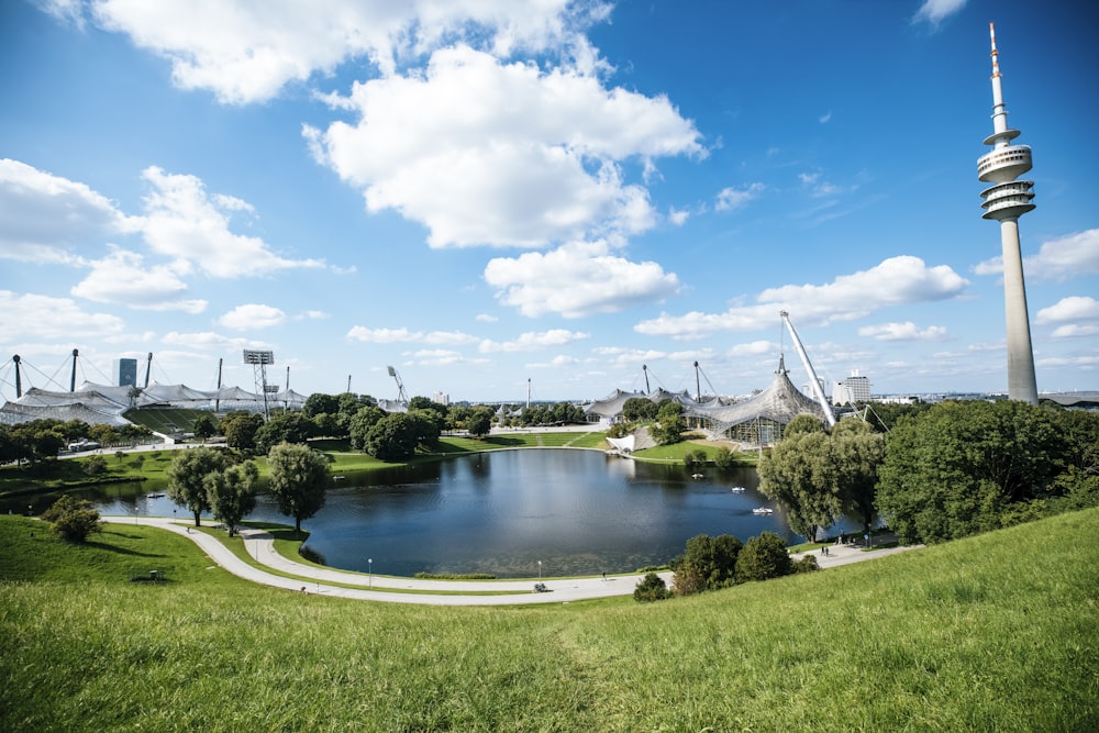 a lake surrounded by a lush green field next to a tall tower