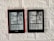 Two Kindle devices are mounted on a textured white wall. Each device displays the same page from a black-and-white manga. The manga panels depict characters having a conversation with some text bubbles containing the words 'Devil' and 'If you're gonna kill me, do it. I'm dead either way.' The Kindle on the left has a red case, while the one on the right has a black case.