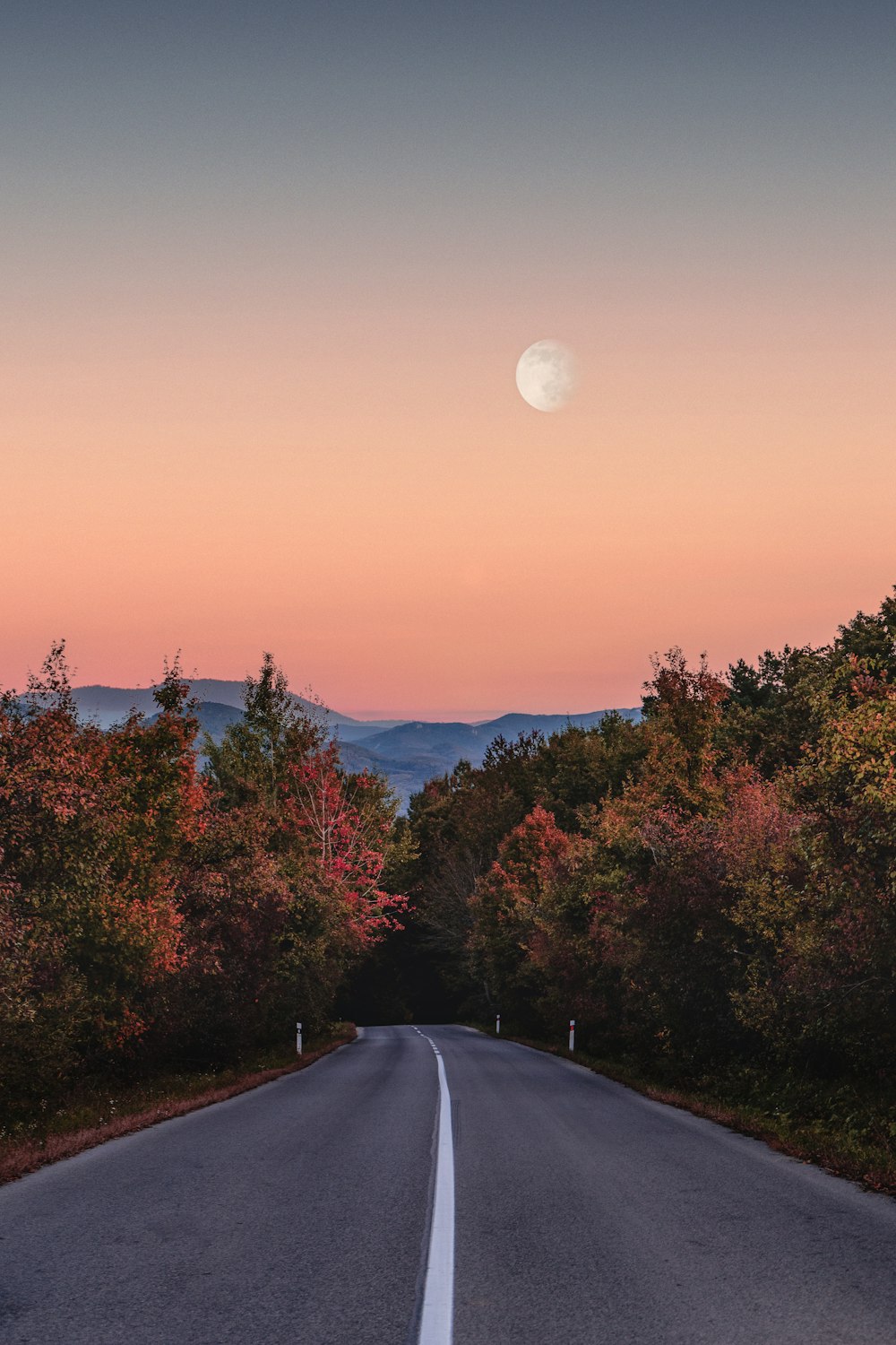 an empty road with a full moon in the distance