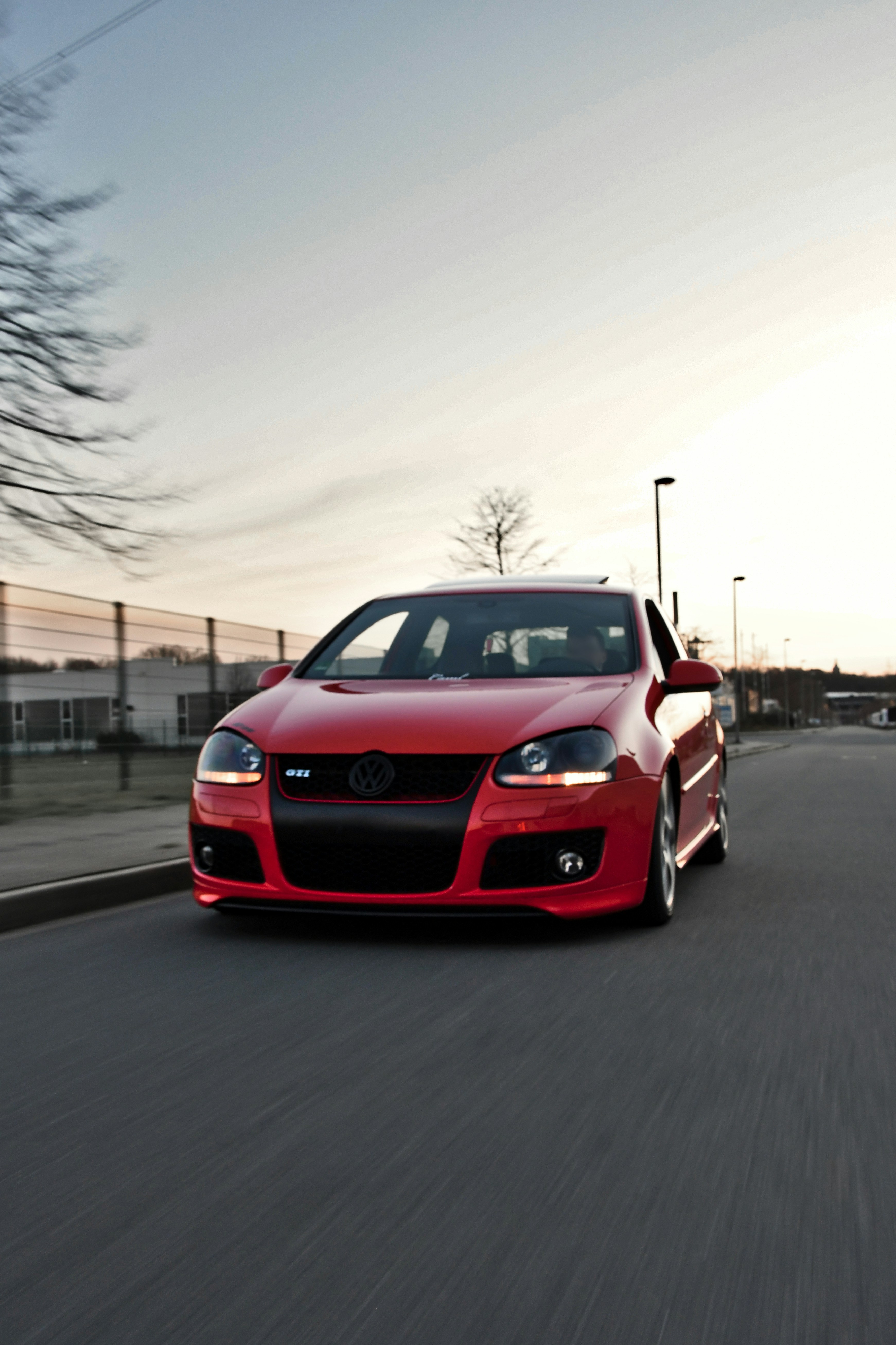 a red car driving down a street next to a parking meter