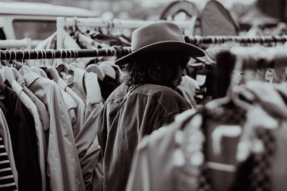 a man in a hat looking at a rack of shirts