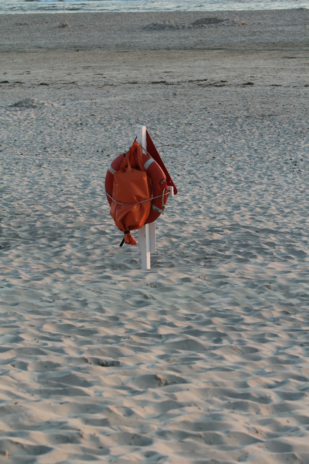 an orange life jacket on a white pole in the sand
