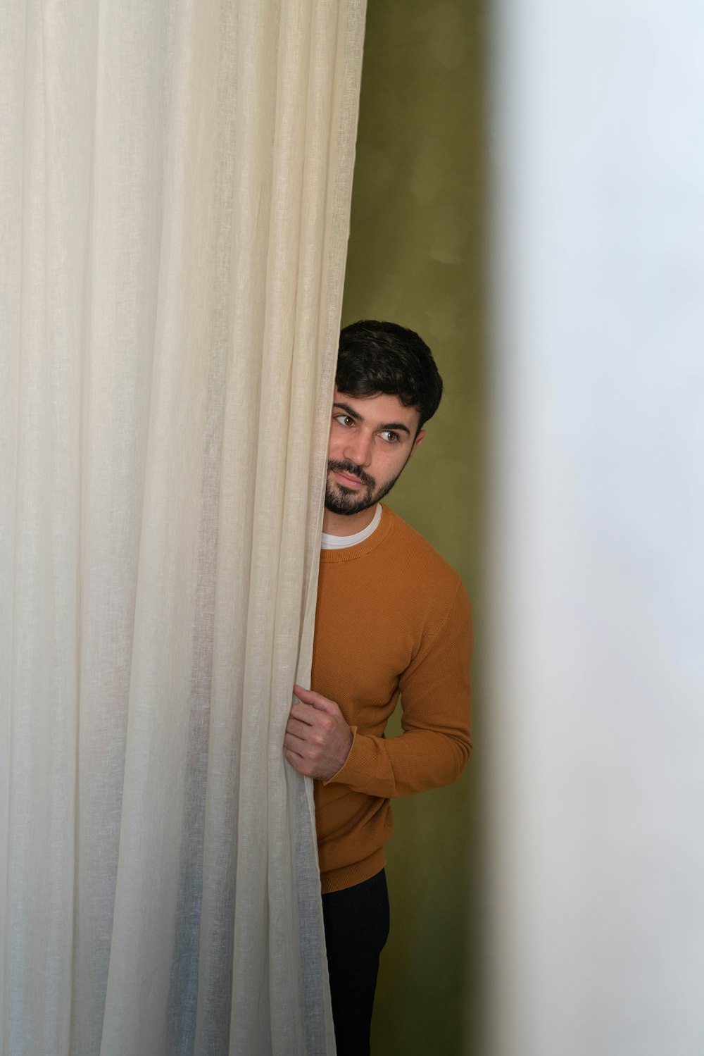 a man peeking out from behind a curtain