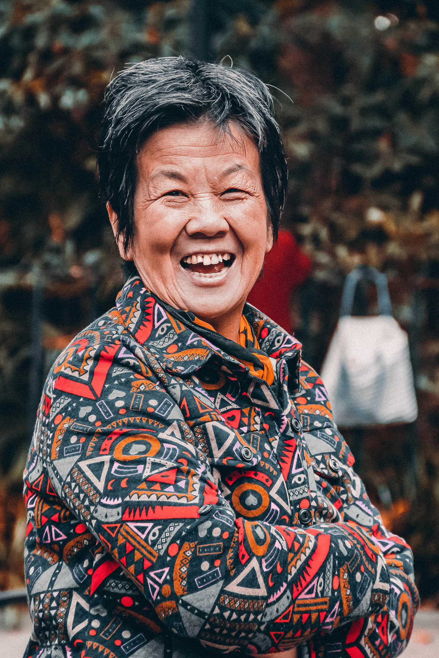 A laughing woman in a patterned jacket at a busy street market