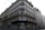 A classic Parisian building with ornate wrought iron balconies and white shutters on multiple floors. The street-level facade is covered in graffiti, and there are bicycles parked at the corner. A person is walking by, adding a sense of urban life to the scene.