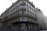 A classic Parisian building with ornate wrought iron balconies and white shutters on multiple floors. The street-level facade is covered in graffiti, and there are bicycles parked at the corner. A person is walking by, adding a sense of urban life to the scene.