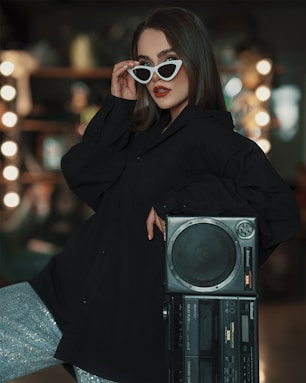 a woman in a black coat and sunglasses holding a boombox
