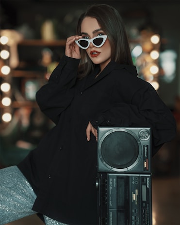 a woman in a black coat and sunglasses holding a boombox