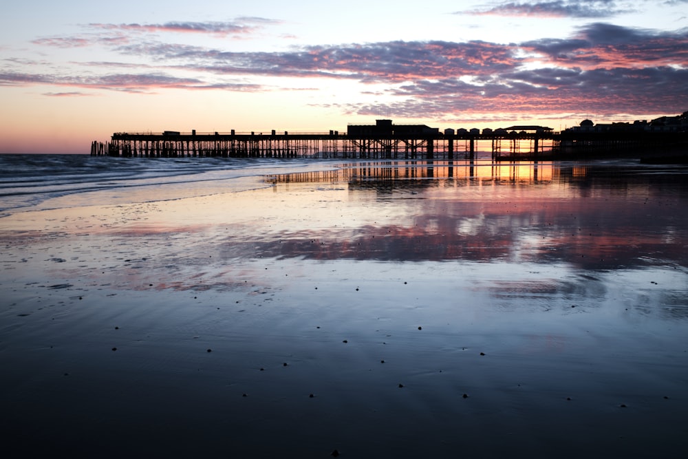 a pier is reflected in the wet sand