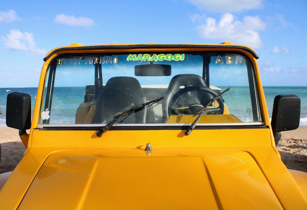 a yellow jeep parked on the beach with the ocean in the background