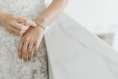 Elegant hands wearing stacked rings and bracelets in gold tones, resting on a marble surface.