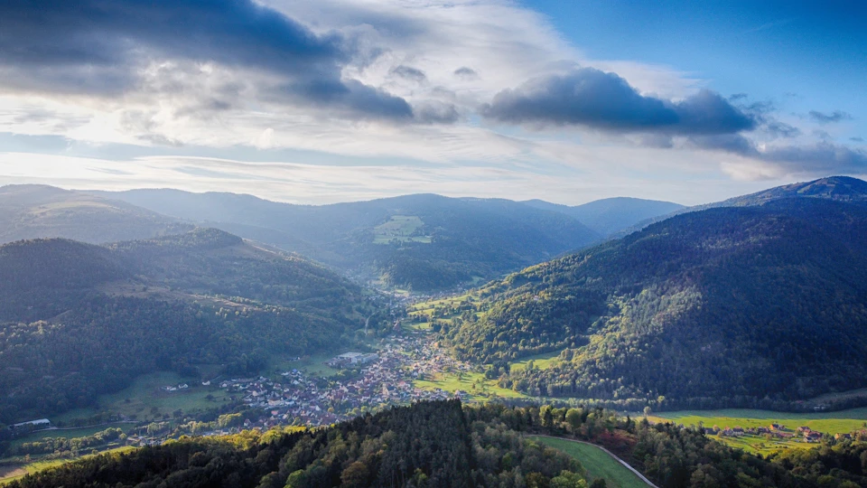 Mountain range with lush green valley and town at its base under clear blue sky