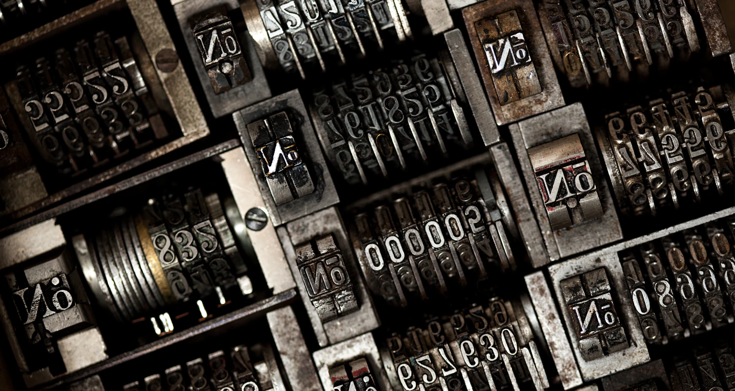 Rows of worn metal numbering type lying face up in a printer's tray