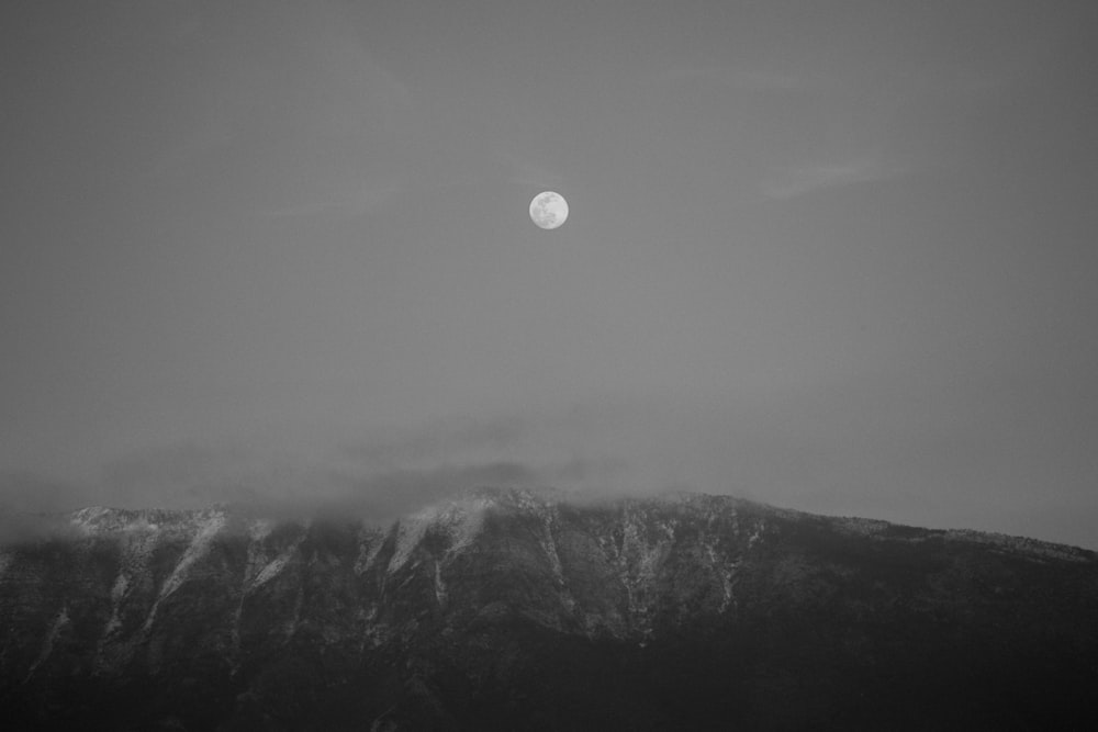 Una foto en blanco y negro de la luna sobre una montaña