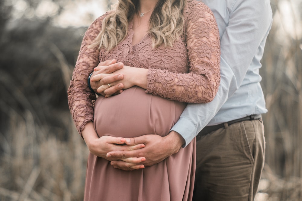 un couple enceinte debout dans un champ, les mains sur le ventre