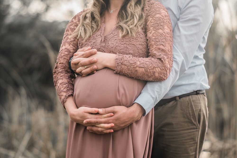 Ein schwangeres Paar steht auf einem Feld mit den Händen auf dem Bauch