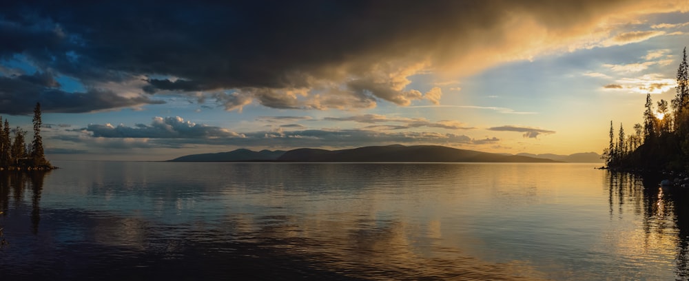 the sun is setting over a lake with trees in the foreground