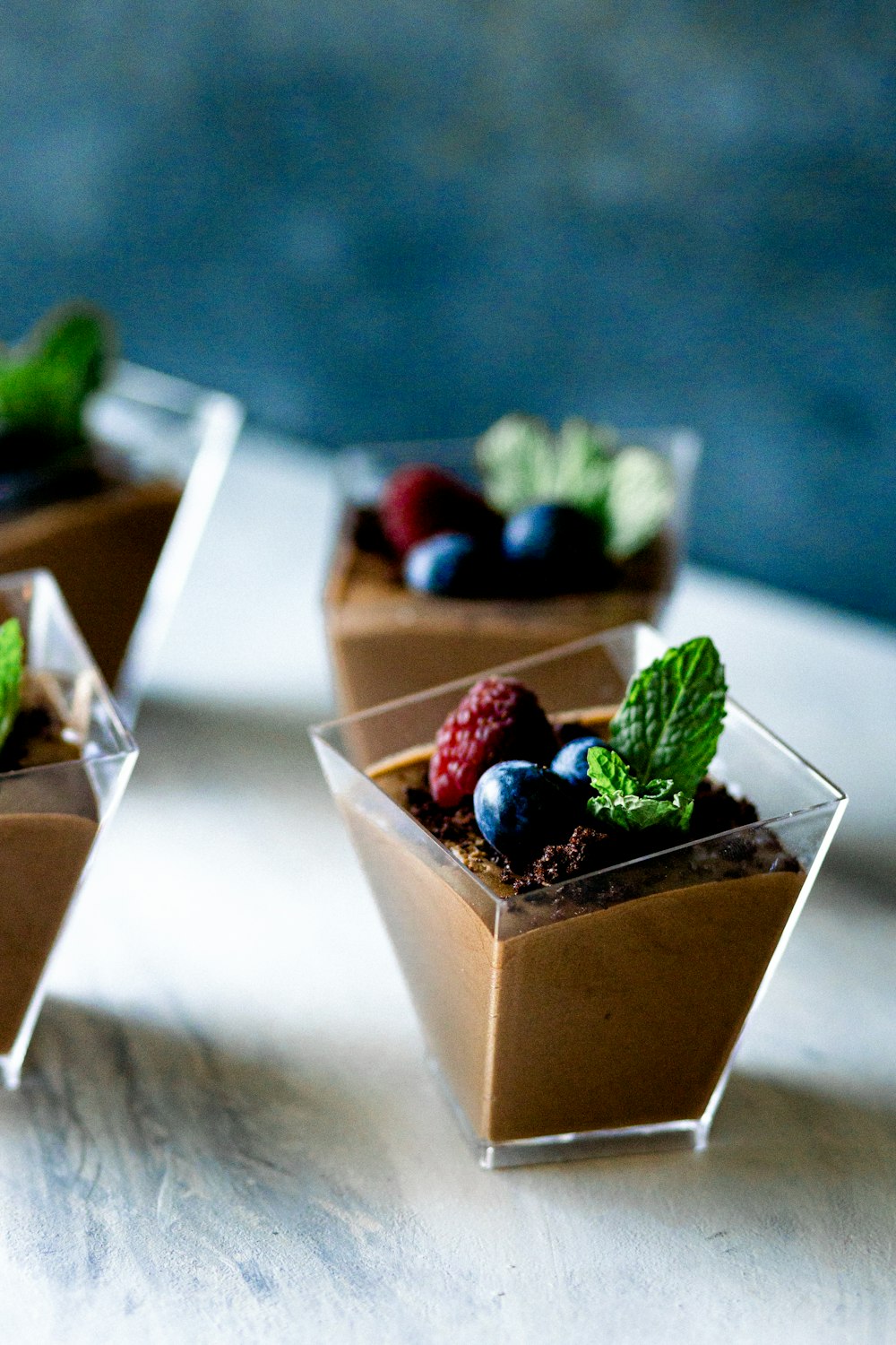 three small desserts with berries and mint on a table