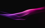 A smooth, flowing wave of vibrant pink and purple light or smoke against a black background, creating a dynamic and ethereal visual effect.